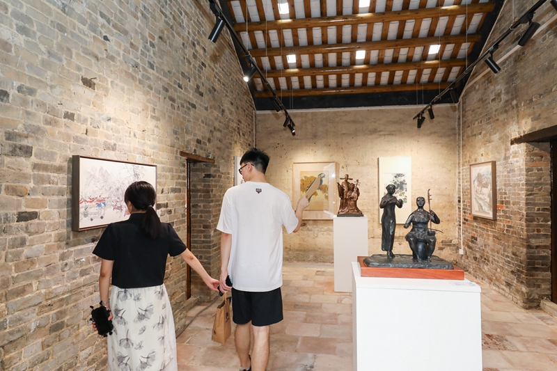 “晴耕雨讀——青苗畫家計劃師生鄉村藝術振興作品展”在廣州市花都區炭步鎮塱頭古村展出，圖為情侶在參觀作品展。受訪者供圖