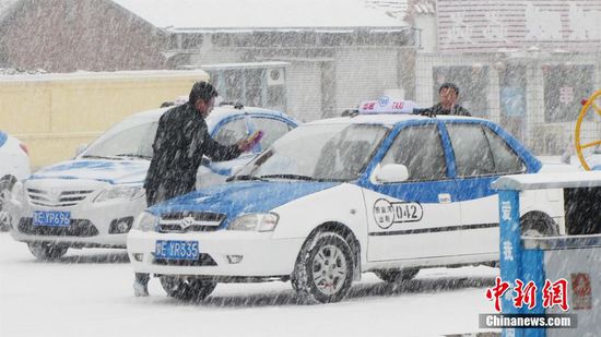 呼倫貝爾市牙克石市圖裏河鎮，一位計程車司機在雪中清理車窗上的積雪。