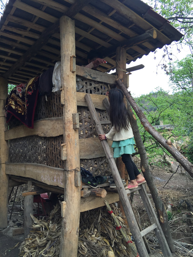 小女孩爬梯子給住在村中包谷垛子高處的吸毒艾滋患者遞火機。(作者供圖)