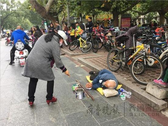 泰安一中北臨，一名乞丐躺在地上，來往市民不時地給他施捨一些零錢。