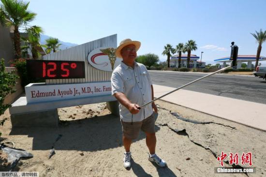 一名棕櫚泉居民在顯示高溫的數字溫度牌前舉起自拍桿。當局稱熱浪“罕見而危險”，會有造成中暑等風險，呼籲民眾避免長時間逗留室外。